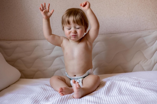 Ein Baby, das mit erhobenen Armen auf einem Bett sitzt