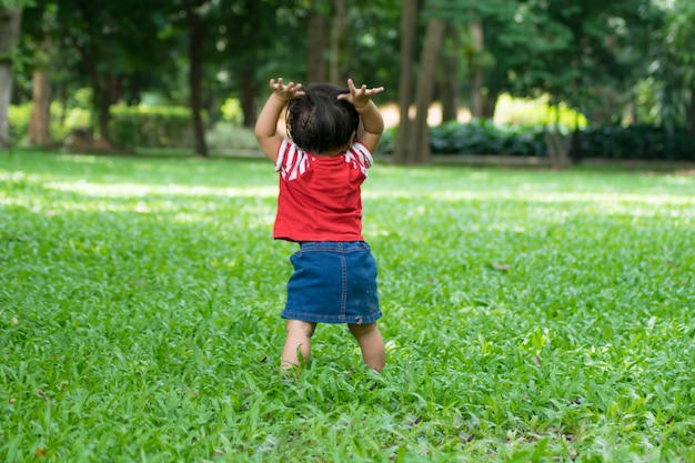 Ein Baby fängt an, zuerst zu gehen und auf grünem Gras zu stehen