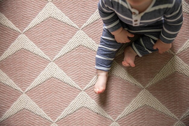 Ein Baby in blauer Kleidung, das zu Hause auf einem Teppich sitzt, wurde von oben erschossen