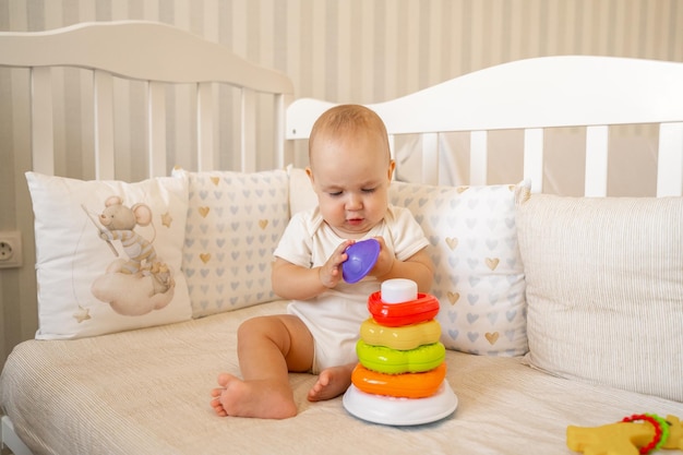 ein Baby in einem Body spielt in einer Krippe mit einer Pyramide