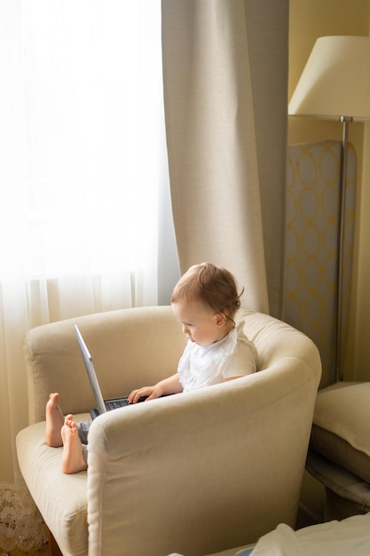 Ein Baby in einem leichten Stuhl sitzt an einem Laptop und verdirbt sein Augenlicht beim Anschauen von Zeichentrickfilmen