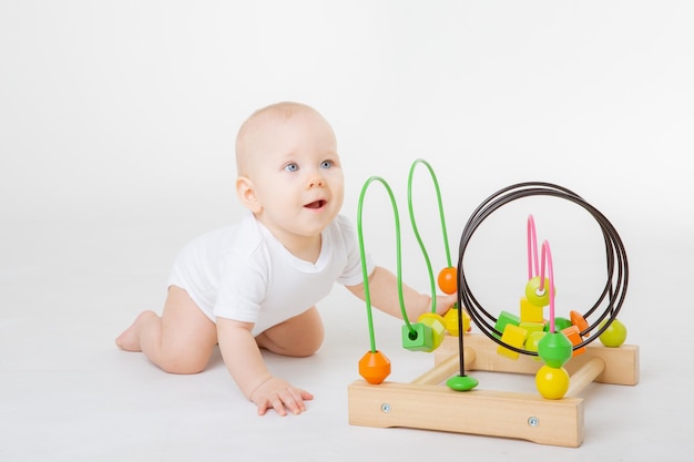 Ein Baby in einem weißen Body spielt mit einem bunten Lernspiel auf weißem Hintergrund