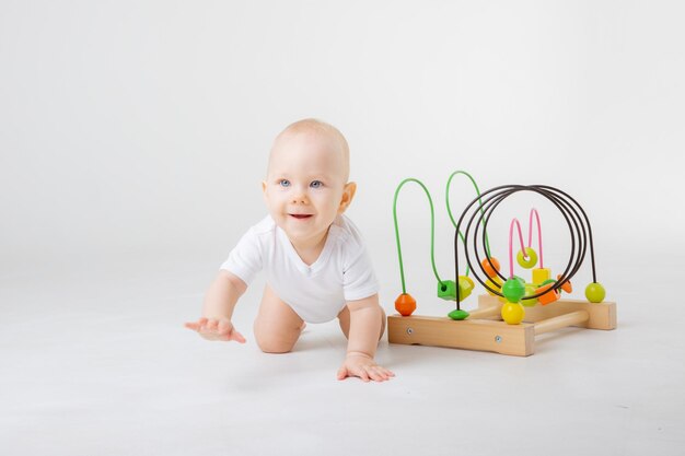 Ein Baby in einem weißen Body spielt mit einem bunten Lernspiel auf weißem Hintergrund