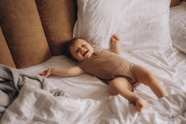 Ein Baby liegt auf einem Bett mit einem Kissen hinter sich.