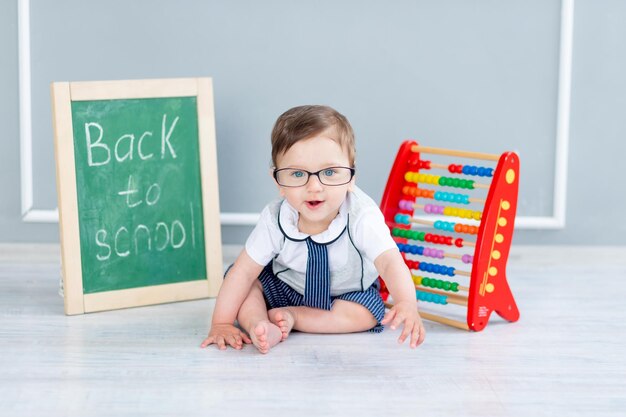 Ein Baby mit Brille und einer Tafel, auf der bald zur Schule steht, sitzt mit Rechnungen
