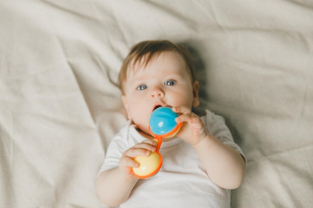 Ein Baby mit einem Zähner und einem Rassel auf einem Baumwollbett Zähnen Kinderartikel Kopierraum