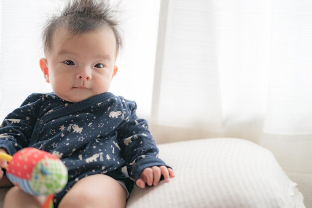 Ein Baby sitzt mit einem Spielzeug in der Hand auf einer Couch.