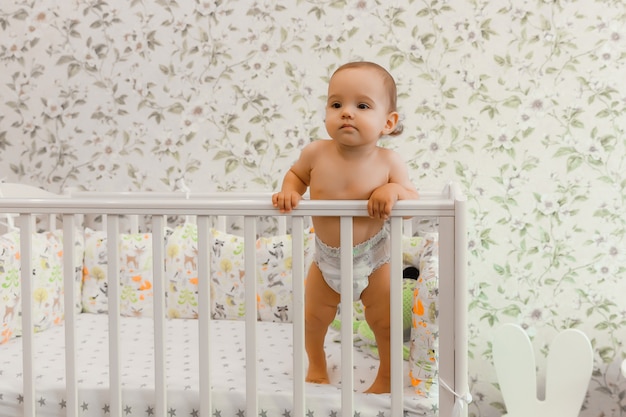 Ein Baby von 11 Monaten in einer Windel steht in seinem Kinderbettchen im Bett