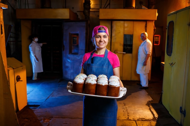 Ein Bäckermädchen hält ein Tablett mit heißem Gebäck in der Bäckerei. Herstellung von Backwaren. Ein Tablett mit frischem knusprigem Gebäck.