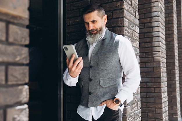 Ein bärtiger grauhaariger Senior benutzt und spricht auf einem Smartphone