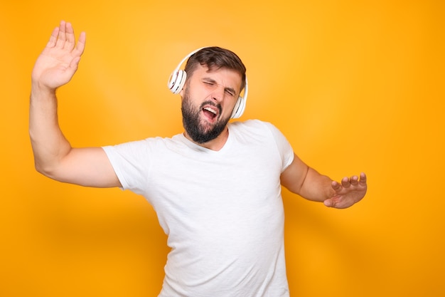 Ein bärtiger Mann im weißen T-Shirt und mit Kopfhörern auf den Ohren tanzt im Rhythmus der Musik.