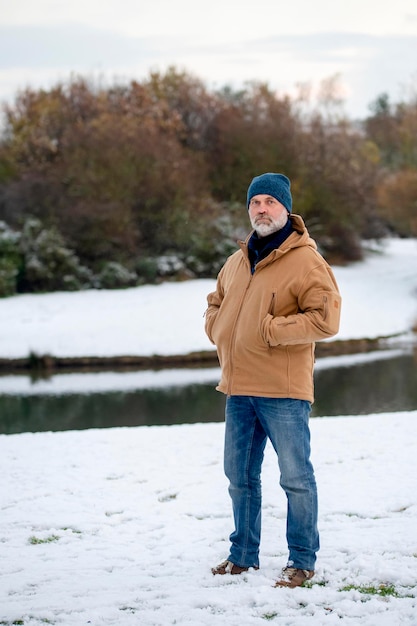 Ein bärtiger Mann in einer Jackenjeans und einem Hut, der an einem verschneiten Wintertag im Park spaziert