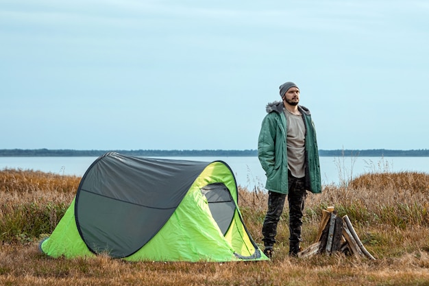 Ein bärtiger Mann nahe einem Campingzelt in der grünen Natur und im See. Reisen, Tourismus, Camping.