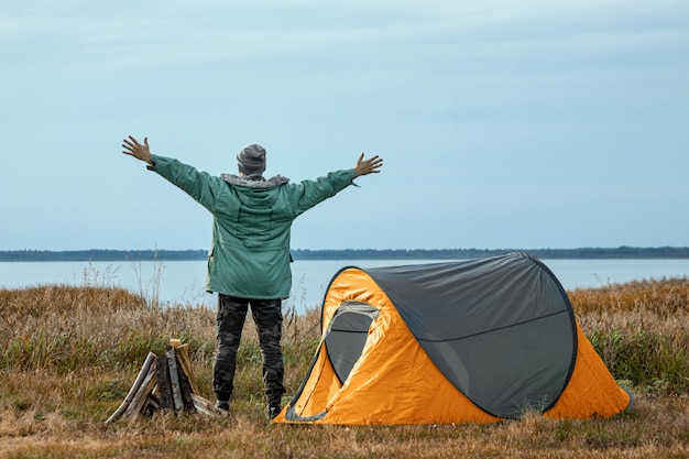 Ein bärtiger Mann nahe einem Campingzelt in der orange Natur und im See. Reisen, Tourismus, Camping.