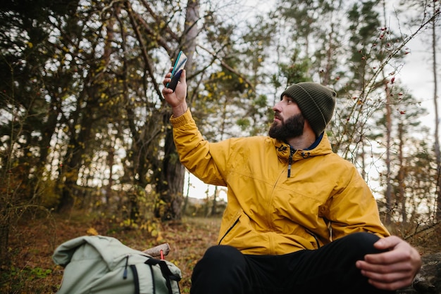 Ein bärtiger Mann ruht sich mitten im Wald auf einem umgestürzten Baum aus Ein Mann nutzt ein Mobiltelefon, um GPS zu suchen