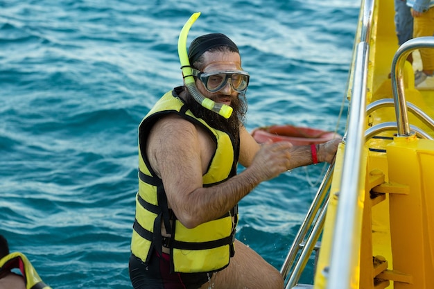 Ein bärtiger Taucher in einer Schwimmweste klettert an Bord eines Bootes im Meer