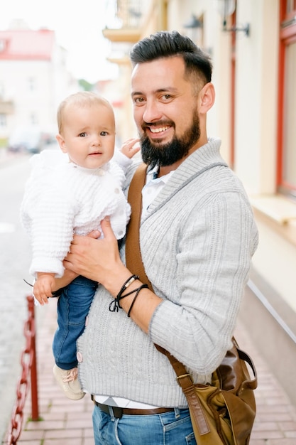 Ein bärtiger Vater mit Brille hält ein Kind und lächelt