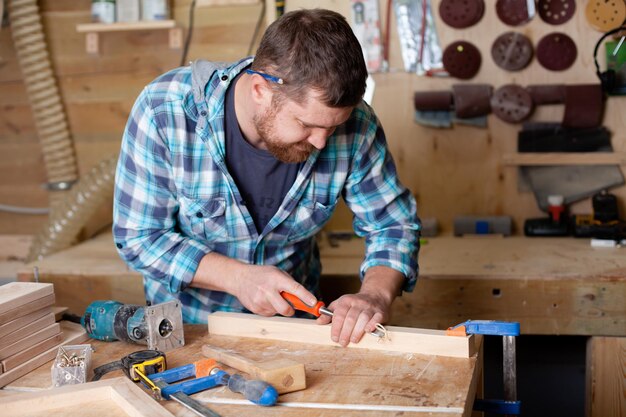 Ein bärtiger Zimmermann im karierten Hemd arbeitet in einer Werkstatt. Holz. Ökologische Verträglichkeit. Lebensstil. Foto in hoher Qualität