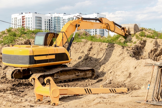 Ein Bagger gräbt eine Baugrube für den Bau eines Wohnhauses. Im Hintergrund neue Wohngebäude. Bauproduktion. Ausgrabung.