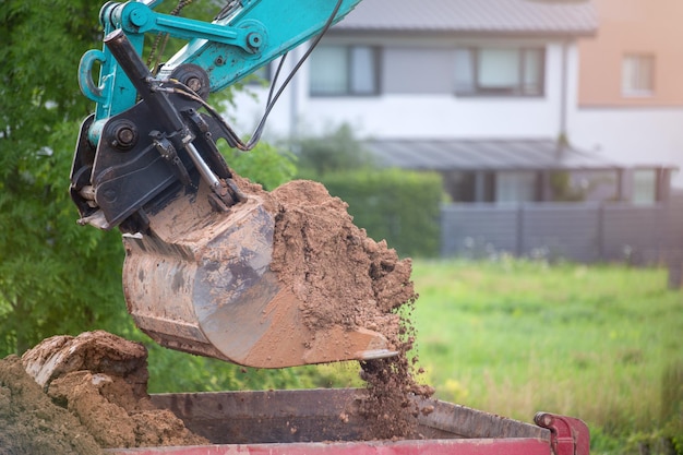 Ein Baggereimer schüttet den Boden auf einen Haufen vor dem Hintergrund eines ländlichen Industriegebiets. Bulldozerarbeiten auf der Baustelle. Hochwertiges Foto