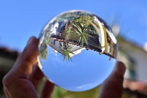 Ein Ball in einer Hand wird in den Himmel gehalten, mit einem Haus im Hintergrund.