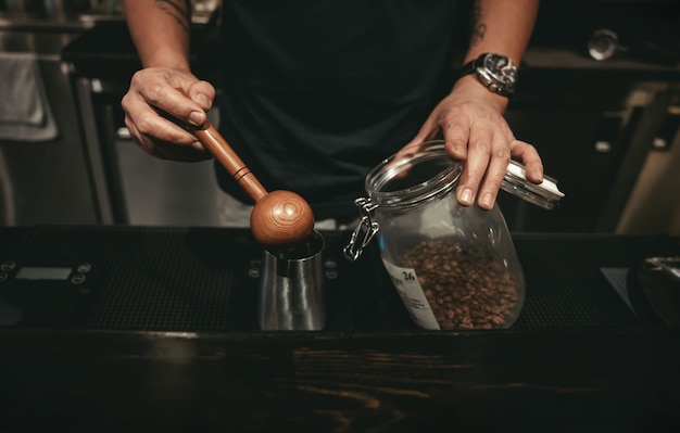 Ein Barista, der im Cafe Kaffee macht. Verwenden eines Holzlöffels zum Messen von Kaffeebohnen