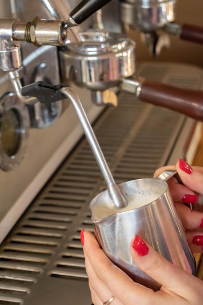 Ein Barista-Mädchen schäumt Milch auf einer Kaffeemaschine auf, um einen Cappuccino oder Latte zuzubereiten. Das Konzept der Getränkezubereitung aus natürlichem Kaffee in Nahaufnahme