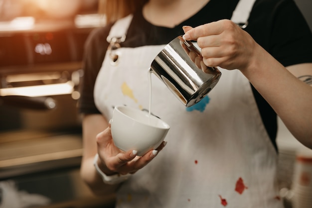 Ein Barista mit einem Metallbecher Milch fertigt eine Latte Art auf einem Kaffee in einem Café an