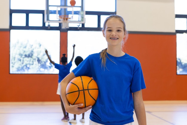 Ein Basketball-Mädchen lächelt im Schulstudio mit Teamkollegen im Hintergrund