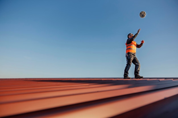 Ein Bauarbeiter spielt mit Helm, während er auf dem Dach steht