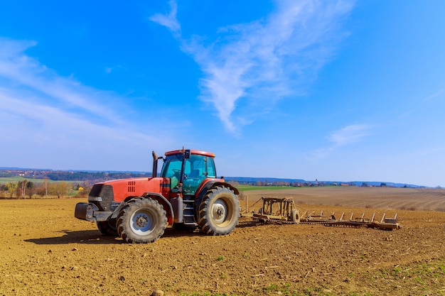 Ein Bauer pflügt den Boden auf dem Feld mit einem Meißelpflug auf einem Traktor. Roter landwirtschaftlicher Traktor mit einem Pflug auf dem Feld.