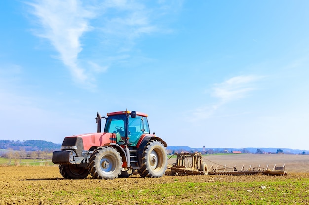 Ein Bauer pflügt den Boden auf dem Feld mit einem Meißelpflug auf einem Traktor. Roter landwirtschaftlicher Traktor mit einem Pflug auf dem Feld.