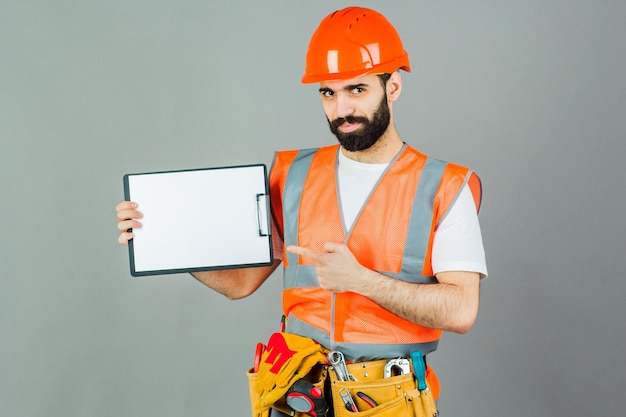 Ein Baumeister in einem orangefarbenen Helm auf grauem Hintergrund unterschreibt etwas