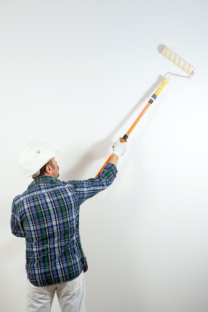 Ein Baumeister mit Schutzhelm streicht mit einer Walze eine weiße Wand