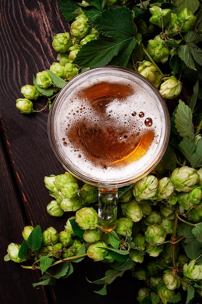 Ein Becher Bier auf einem Holztisch mit einem Zweig frischer Hopfen, rustikal, ohne Menschen.