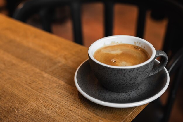 Ein Becher schwarzes Kaffee an der Kante eines Holztisches in einem Café-Coffee-Shop mit Kopierplatz