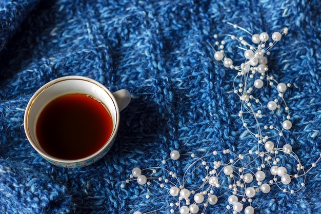 Ein becher tee auf einem blauen strickhintergrund, die ruhige zeit, herbststimmung.