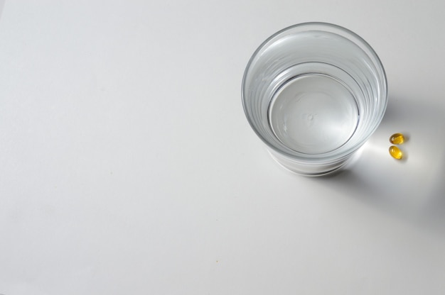 Ein Becherglas und zwei gelbe Tabletten mit Vitaminen. Nahaufnahme.