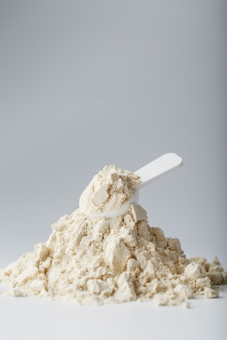 Foto ein berg von sojaproteinisolat in pulverform mit einem messlöffel auf weißem hintergrund.