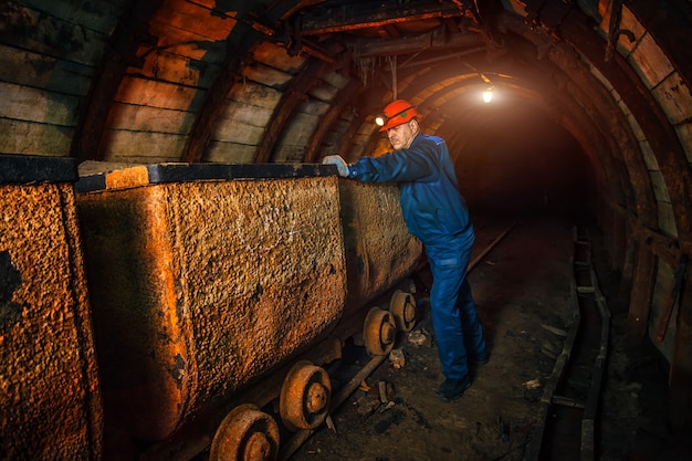 Ein Bergmann in einer Kohlengrube steht in der Nähe eines Wagens. Kopieren Sie Platz.