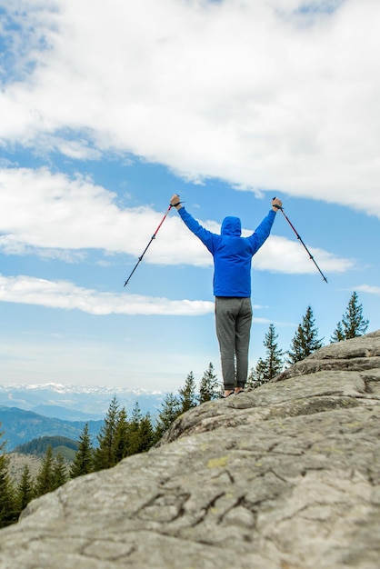 Ein Bergsteiger steht hoch in den Bergen gegen den Himmel und feiert den Sieg mit erhobenen Händen
