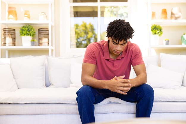 Ein besorgter, trauriger Mann zweier Rassen sitzt auf dem Sofa im Wohnzimmer und denkt an Kopierraum, Emotionen, Depressionen, Lebensstil und häusliches Leben.