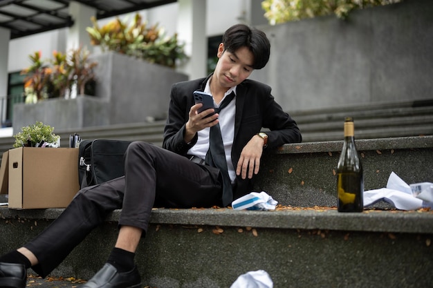 Ein betrunkener und hoffnungsloser arbeitsloser asiatischer Geschäftsmann sitzt auf der Treppe vor dem Gebäude