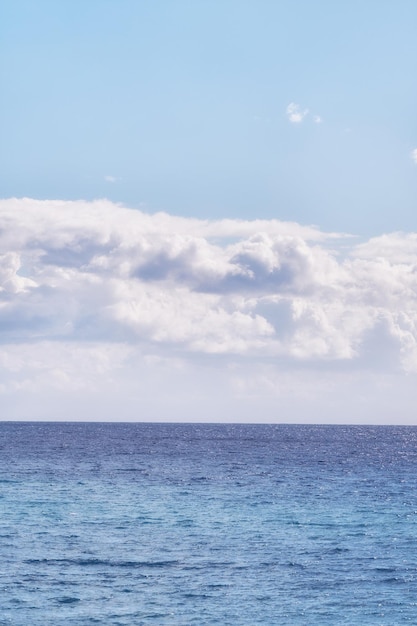 Ein bewölkter blauer Himmel und ein friedlicher, ruhiger Ozean, getrennt durch einen schönen Horizont mit Kopierbereich. Tiefblaues Wasser unter einer Wolkengebilde-Skyline