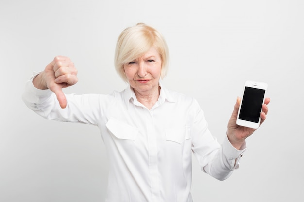 Ein Bild der reifen Dame mit neuem Smartphone. Sie hat es getestet und zugegeben, dass dieses Telefon schlecht ist. Deshalb zeigt sie einen großen Daumen nach unten.