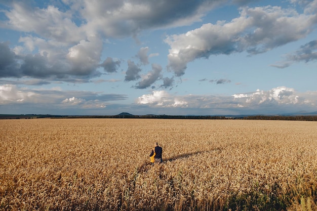 Ein Bild von einer Drohne mit einem Vater und einem Sohn, die zwischen einem goldenen Weizenfeld stehen und die Berge und Bäume bewundern.