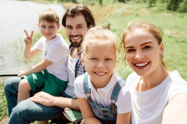 Foto ein bild von einer familie, die zusammen am rand des flussufers sitzt. sie schauen gerade und lächeln. junge zeigt stücksymbol.
