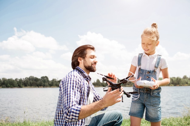 Ein Bild von Vater und Tochter, die Zeit miteinander verbringen. Guy hält eine Drohne und zeigt sie dem Mädchen, während ein kleines Kind ein Bedienfeld in der Hand hat. Das Kind schaut auch auf die Drohne.
