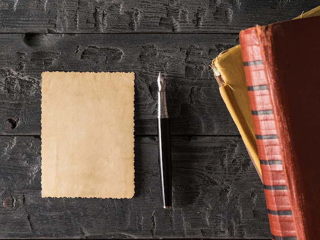 Ein Blatt altes Papier und ein Füllfederhalter mit Büchern auf einem Holztisch. Retro Schreibpapier. Flach liegen Der Blick von oben.