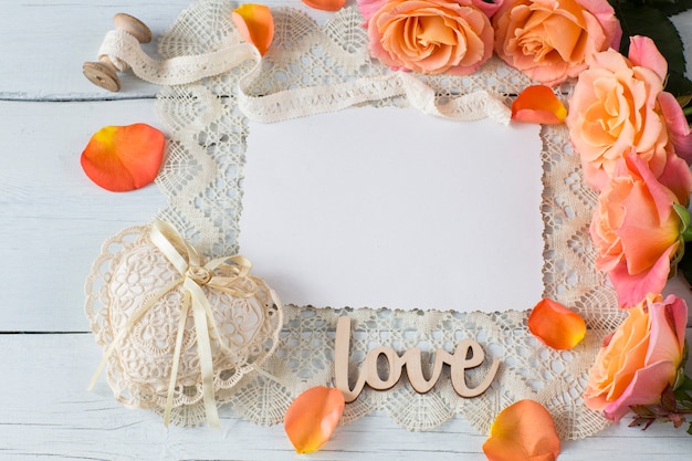 ein Blatt Papier, orange Rosen, ein Herz aus Spitze, Rosenblüten und Spitze